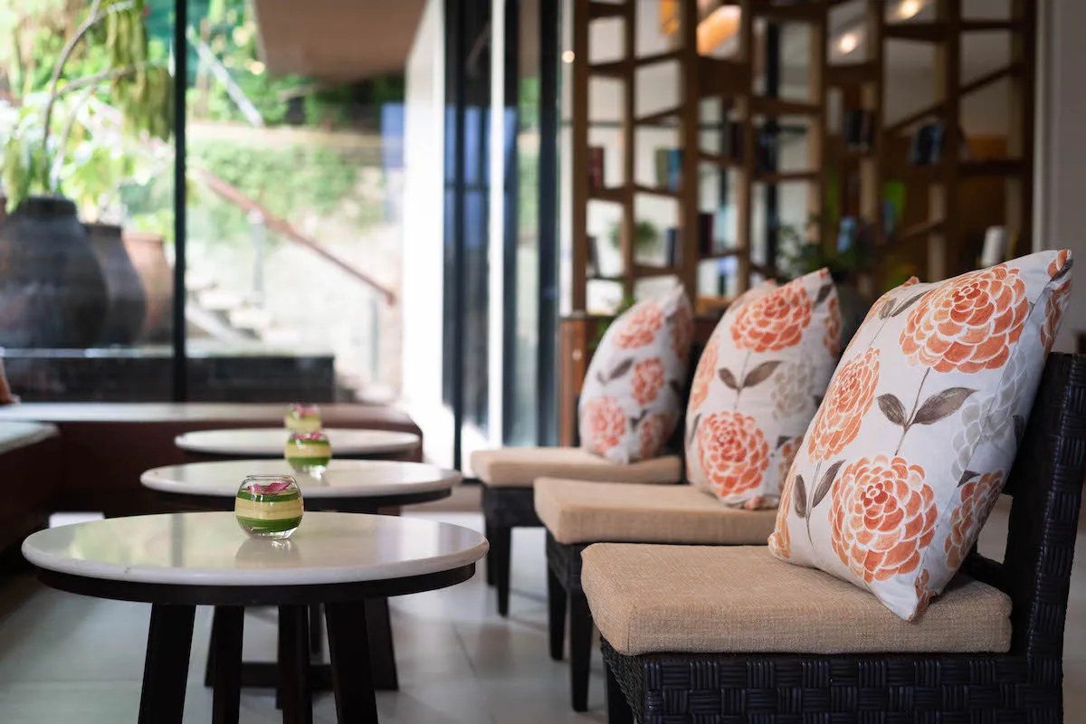 Cosy seating area at Peach Blossom Resort Phuket with floral cushions and small round tables decorated with floating flower bowls in a bright modern lounge setting