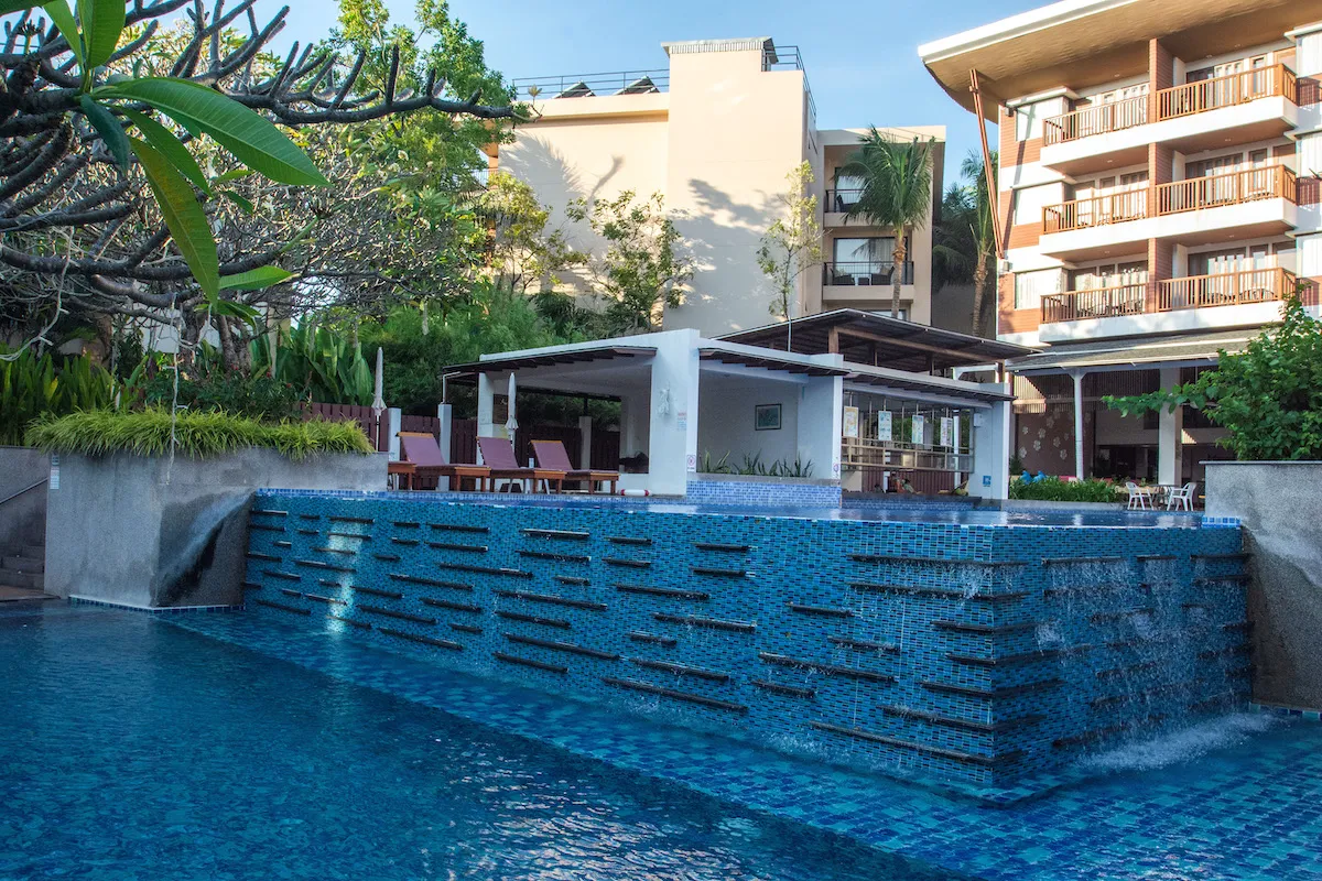 Multi-level swimming pool with cascading water feature and sun loungers at Peach Blossom Resort Phuket surrounded by tropical greenery and modern resort buildings