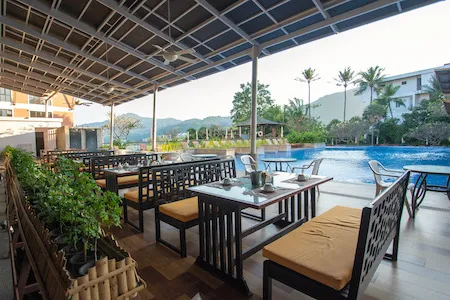 Outdoor dining area with cushioned seating beside a large swimming pool overlooking palm trees and mountains