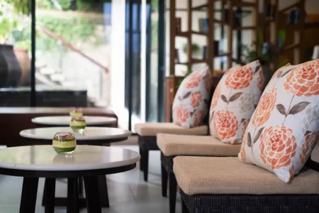 Cosy seating area at Peach Blossom Resort Phuket with floral cushions and small round tables decorated with floating flower bowls in a bright modern lounge setting